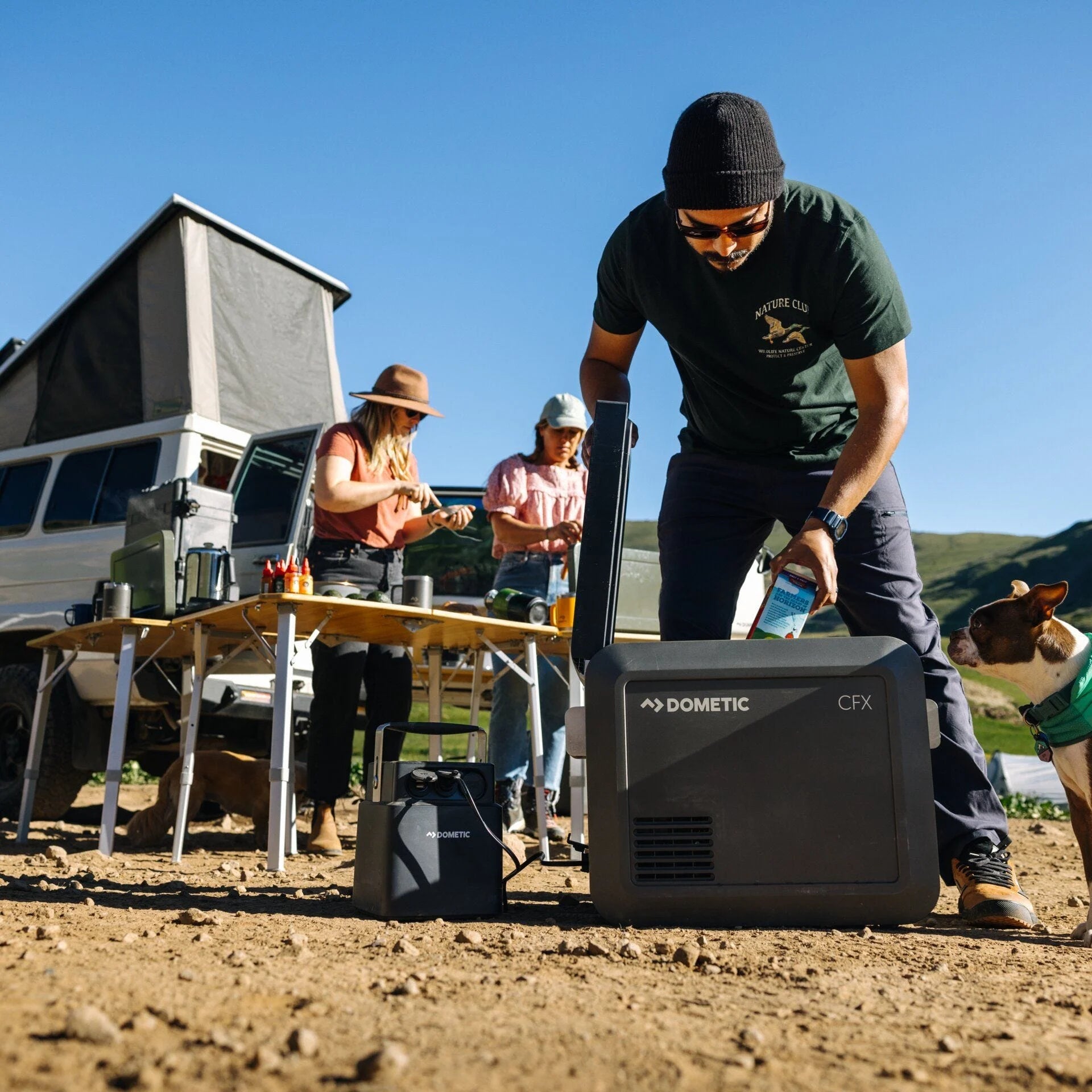 Person using a Dometic CFX generator outdoors with a van and people in the background.